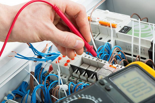 Hand of an electrician with multimeter probe at an electrical switchgear cabinet