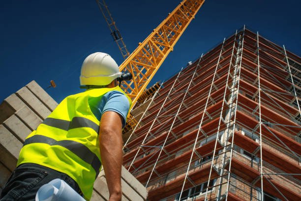 Closeup construction engineer standing in front of a building. He's doing some calculation and inspection by looking at construction plan and using binoculars.